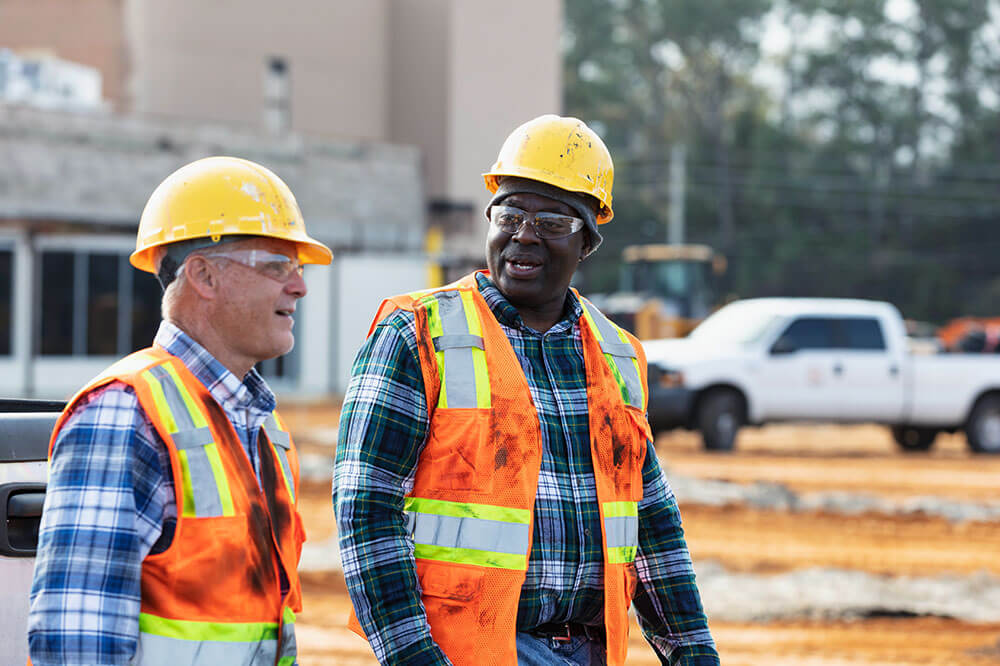 two men in high vis vest and hardhats, walking and talking
